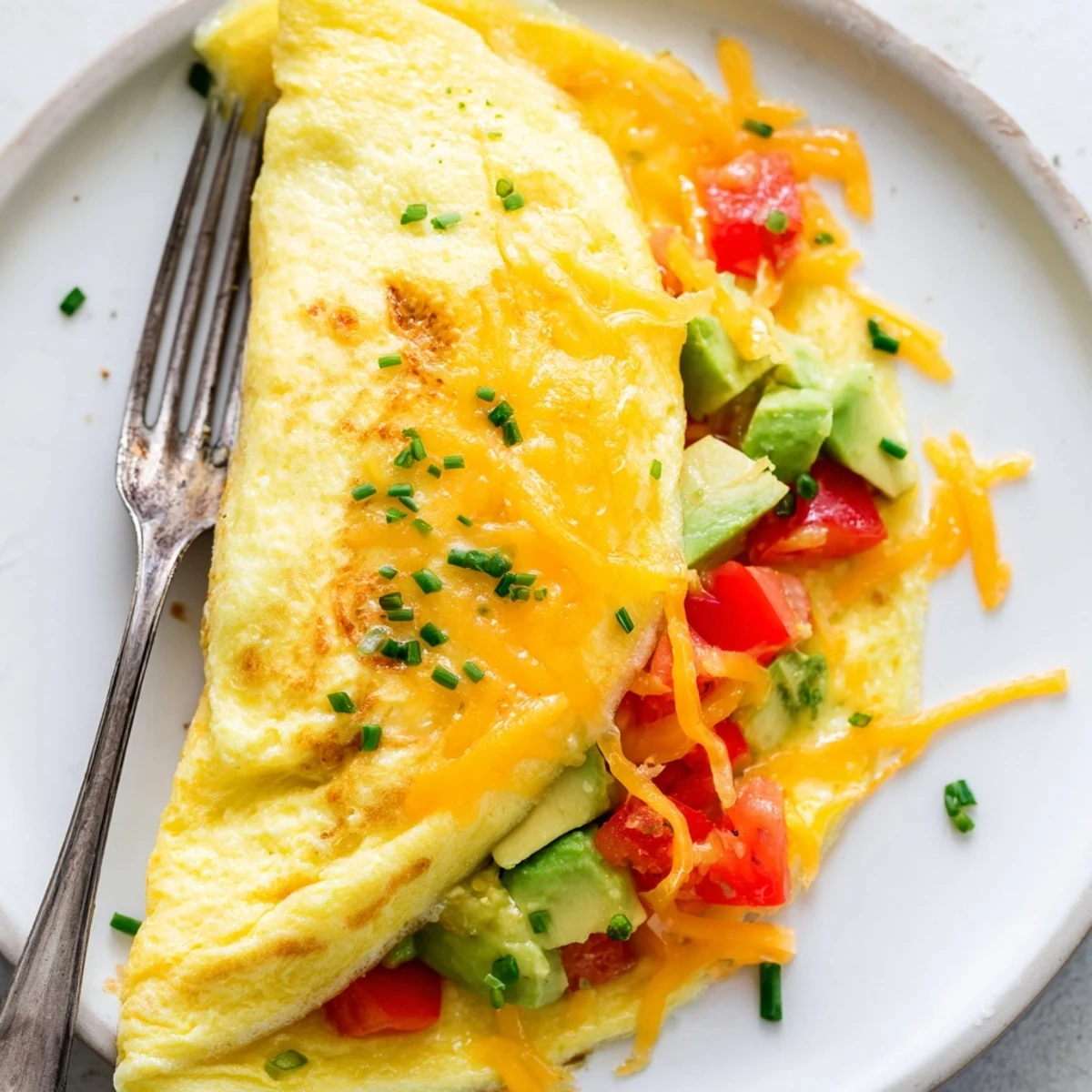 Golden avocado cheesy tomato omelette folded over melted cheddar on a white plate