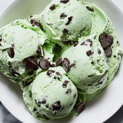 Close-up scoop of Green Mint Chocolate Chip Ice Cream showing a vibrant green hue and rich chocolate chunks in a waffle cone.