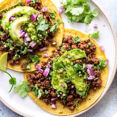 Warm corn tortillas cradle juicy, cumin-spiced ground beef, topped with vibrant salsa verde, cilantro, and a hint of lime.  