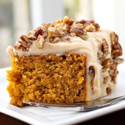 Golden pumpkin pecan cake topped with swirled cinnamon cream cheese icing and scattered toasted nuts